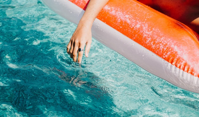 Resort-style swimming pool woman dangles her hand in the pool as she floats in an inflatable vessel